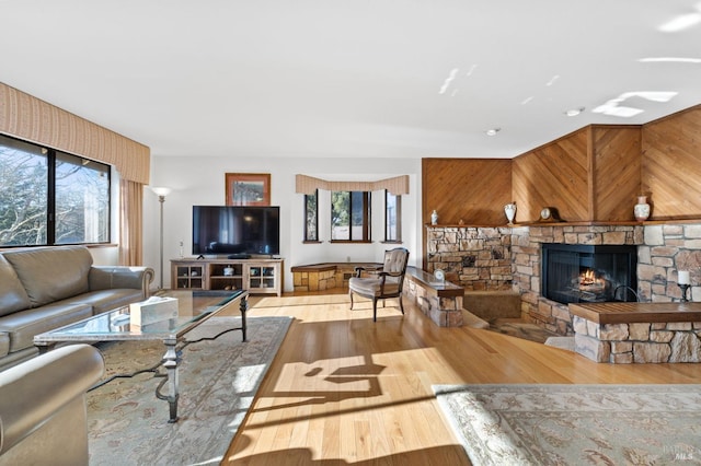 living room with wood walls, light wood-type flooring, and a stone fireplace