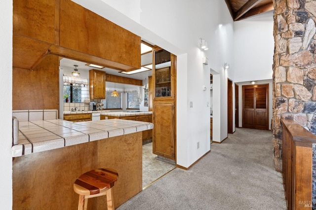 kitchen featuring a high ceiling, light colored carpet, kitchen peninsula, a breakfast bar, and tile countertops