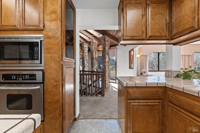 kitchen with light carpet, tile countertops, kitchen peninsula, and appliances with stainless steel finishes