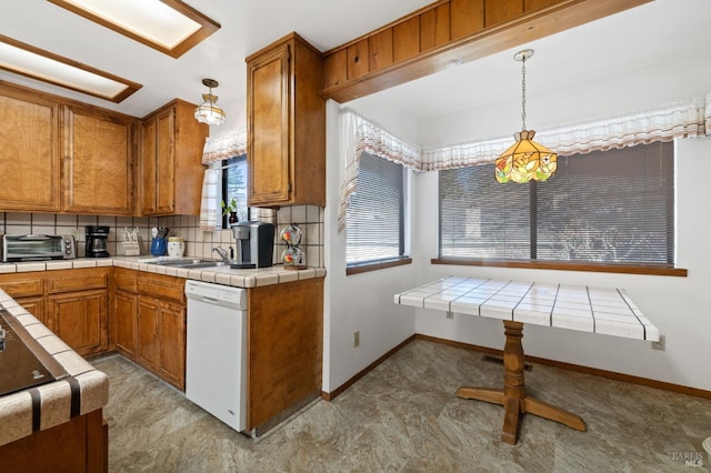 kitchen featuring kitchen peninsula, pendant lighting, white dishwasher, backsplash, and tile countertops