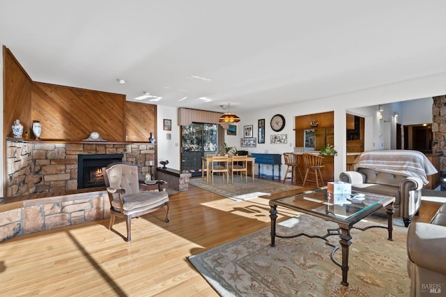 living room featuring a stone fireplace, wood walls, and wood-type flooring