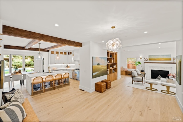 living room with sink, an inviting chandelier, a high end fireplace, beam ceiling, and light hardwood / wood-style floors