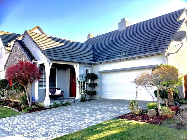 ranch-style home featuring a garage, a chimney, decorative driveway, a porch, and stucco siding