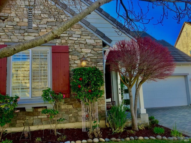 view of property exterior featuring a garage, stone siding, and decorative driveway