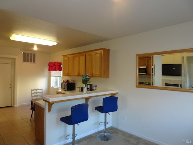 kitchen featuring light tile patterned floors, a kitchen breakfast bar, and kitchen peninsula