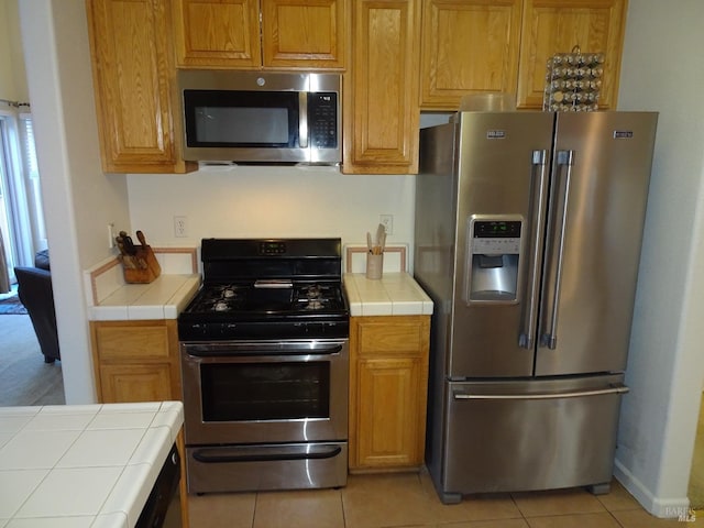 kitchen with stainless steel appliances, tile counters, and light tile patterned floors