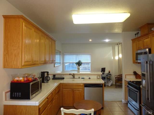 kitchen featuring stainless steel appliances, sink, tile counters, and light tile patterned floors