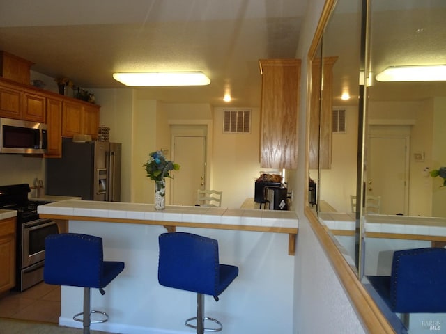 kitchen featuring light tile patterned flooring, appliances with stainless steel finishes, tile counters, and a kitchen breakfast bar