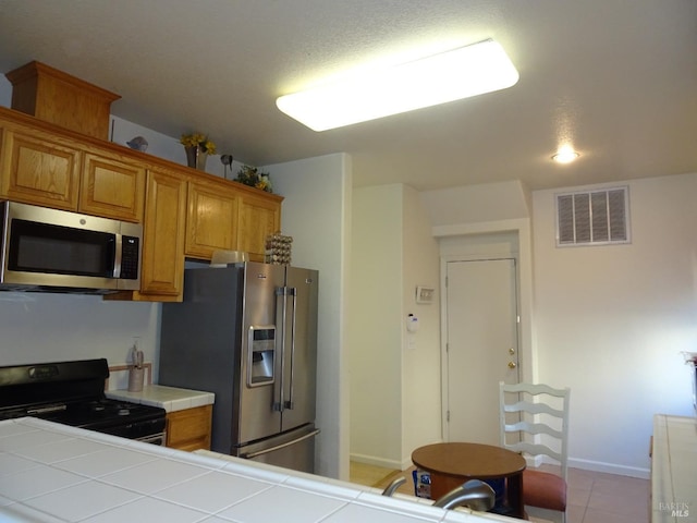 kitchen featuring light tile patterned floors, tile countertops, and appliances with stainless steel finishes