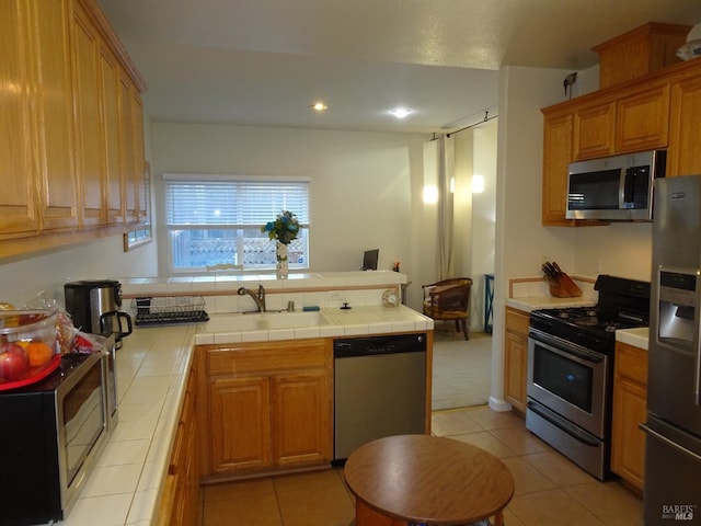 kitchen featuring stainless steel appliances, light tile patterned flooring, sink, and tile countertops