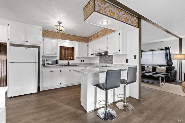 kitchen with kitchen peninsula, a kitchen breakfast bar, white refrigerator, white cabinets, and light stone countertops