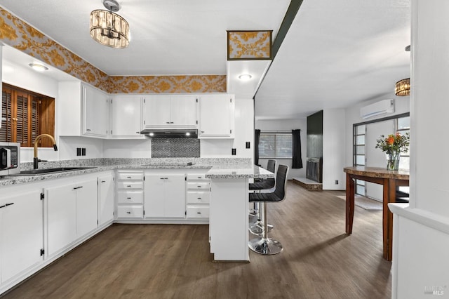 kitchen featuring white cabinets, a wall mounted AC, pendant lighting, and sink