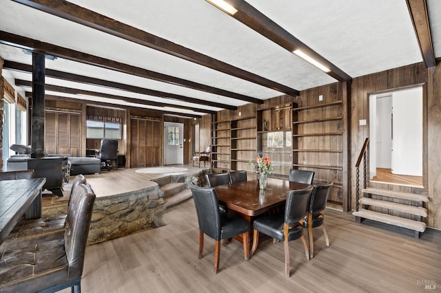 dining area featuring wood walls, light hardwood / wood-style flooring, beam ceiling, and a wood stove