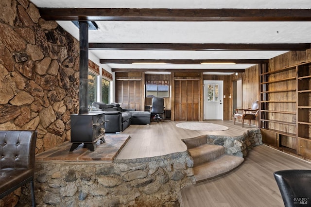 living room with a wood stove, wood-type flooring, wood walls, and beamed ceiling