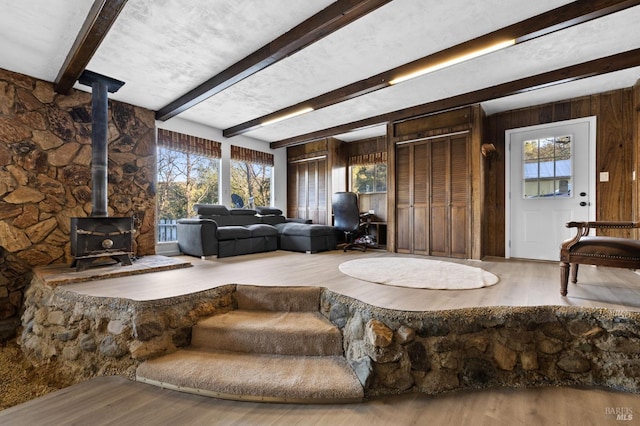 living room with a wood stove, beamed ceiling, wood walls, and wood-type flooring