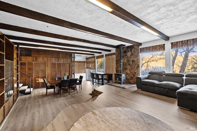 living room with wood walls, light hardwood / wood-style floors, beam ceiling, and a wood stove