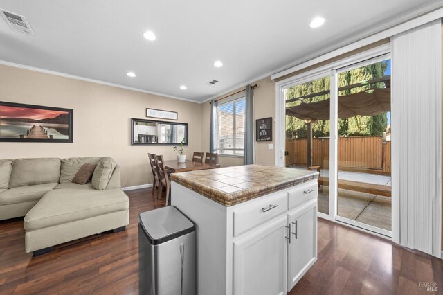 kitchen featuring visible vents, tile counters, white cabinets, ornamental molding, and open floor plan