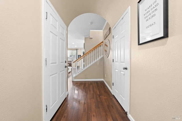 entrance foyer featuring baseboards, arched walkways, dark wood finished floors, a textured wall, and stairs