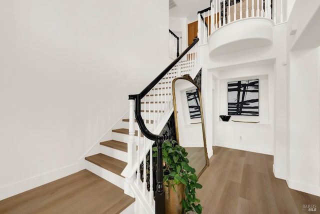 stairway with hardwood / wood-style floors and a towering ceiling