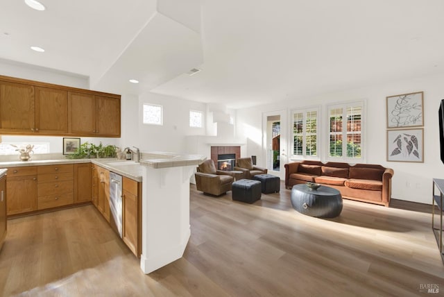 kitchen featuring dishwasher, sink, kitchen peninsula, light wood-type flooring, and a tiled fireplace