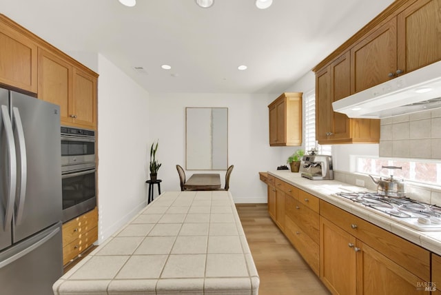 kitchen featuring decorative backsplash, tile counters, light hardwood / wood-style floors, and stainless steel appliances