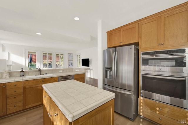 kitchen with a center island, sink, hardwood / wood-style flooring, stainless steel appliances, and tile counters