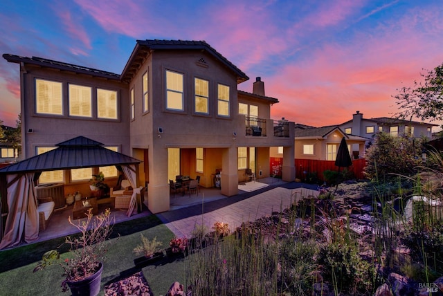 back house at dusk featuring a balcony, a gazebo, central AC unit, and a patio