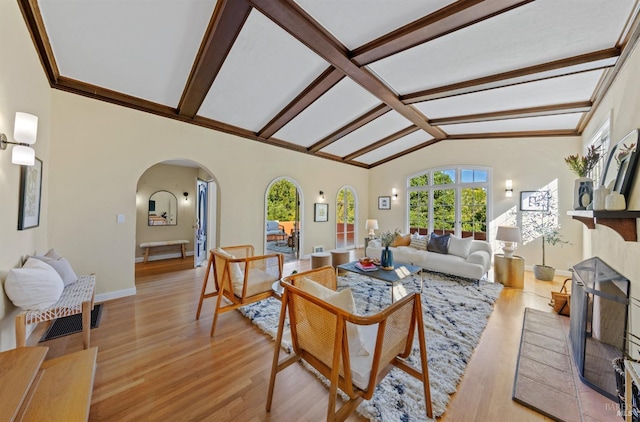 living area with arched walkways, vaulted ceiling with beams, a fireplace with raised hearth, visible vents, and light wood-type flooring