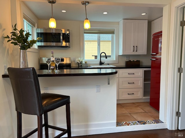 kitchen with a breakfast bar, white cabinetry, sink, hanging light fixtures, and stainless steel appliances