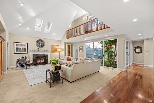 living room featuring a high end fireplace, a skylight, a towering ceiling, and light hardwood / wood-style flooring