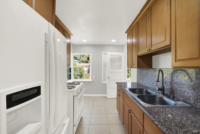 kitchen with sink, white appliances, tasteful backsplash, light tile patterned flooring, and dark stone counters