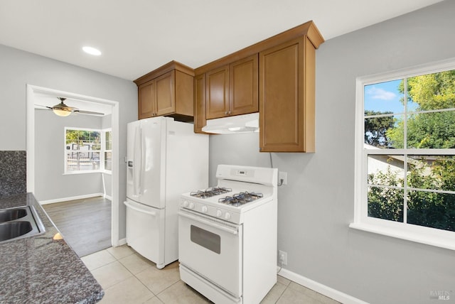 kitchen featuring dark stone countertops, light tile patterned floors, white appliances, and ceiling fan