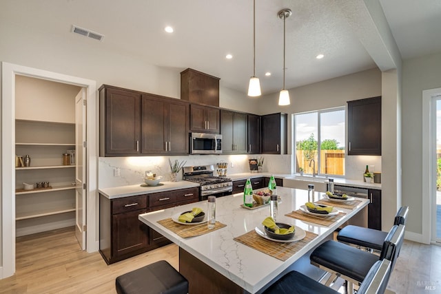 kitchen with light stone countertops, a kitchen island, a kitchen bar, decorative light fixtures, and stainless steel appliances