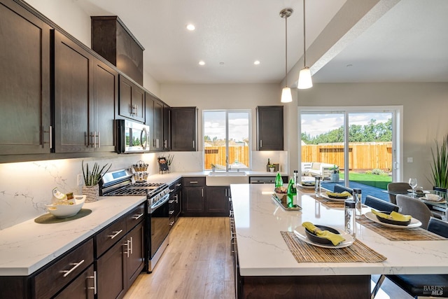 kitchen featuring decorative light fixtures, appliances with stainless steel finishes, light stone counters, and a center island