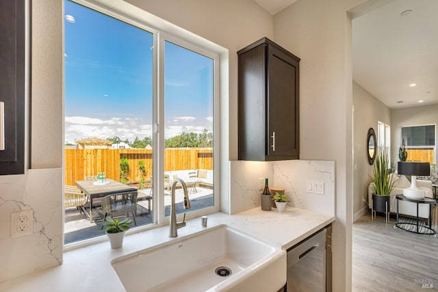 interior space with tasteful backsplash, light hardwood / wood-style floors, sink, stainless steel dishwasher, and dark brown cabinets