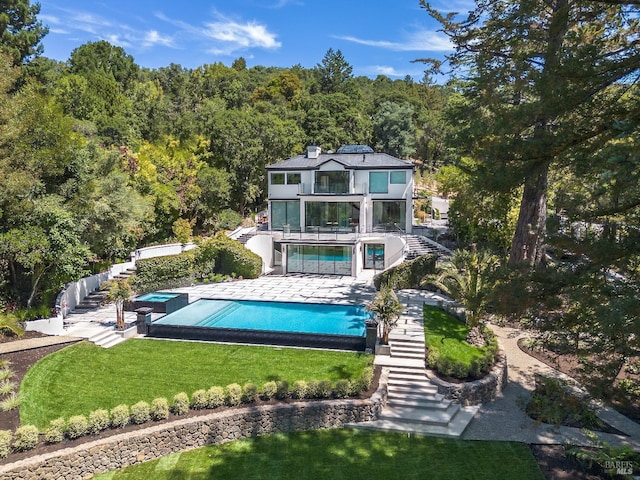 back of property with a swimming pool with hot tub, a yard, a balcony, and a patio