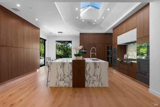 kitchen with a kitchen bar, sink, stainless steel gas cooktop, a skylight, and a large island