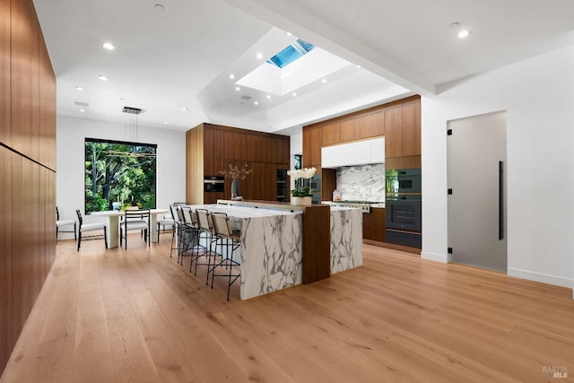 kitchen with backsplash, a spacious island, oven, a kitchen bar, and light wood-type flooring