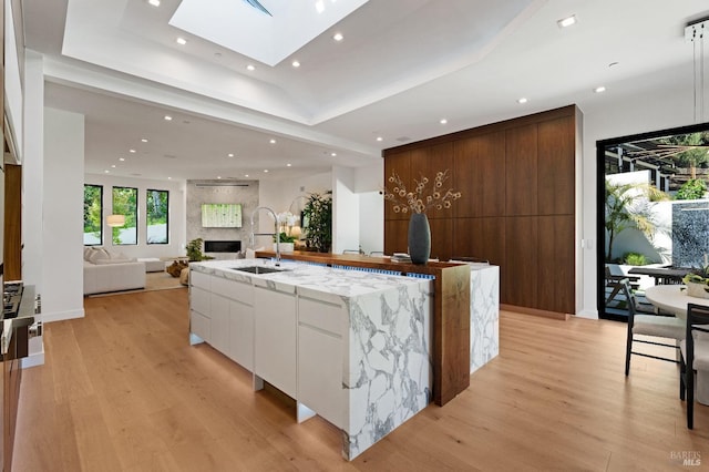 kitchen with light wood-type flooring, white cabinetry, sink, and a kitchen island with sink