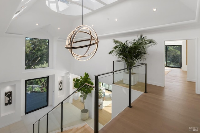 interior space featuring a towering ceiling, wood finished floors, a chandelier, and a skylight