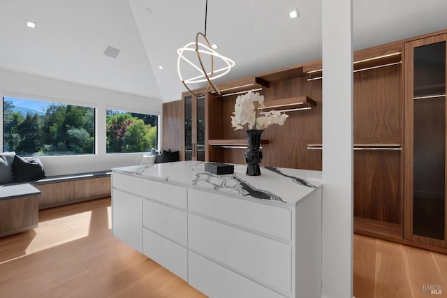 spacious closet featuring light hardwood / wood-style floors, lofted ceiling, and a notable chandelier