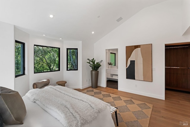 bedroom with ensuite bathroom, light wood-type flooring, and lofted ceiling