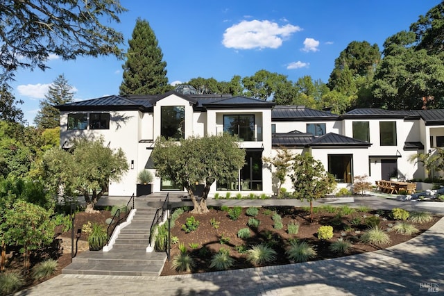 modern home with stairs, stucco siding, metal roof, and a standing seam roof