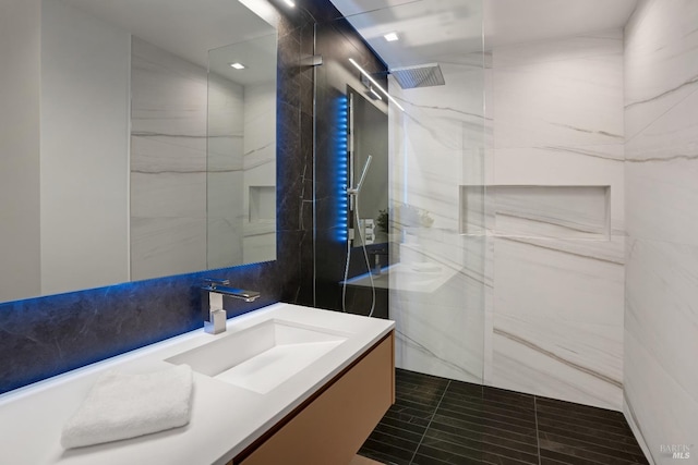 full bath featuring vanity, a marble finish shower, tile patterned flooring, and tile walls