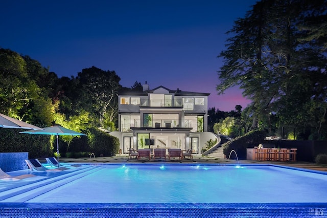 pool at dusk featuring pool water feature and a patio