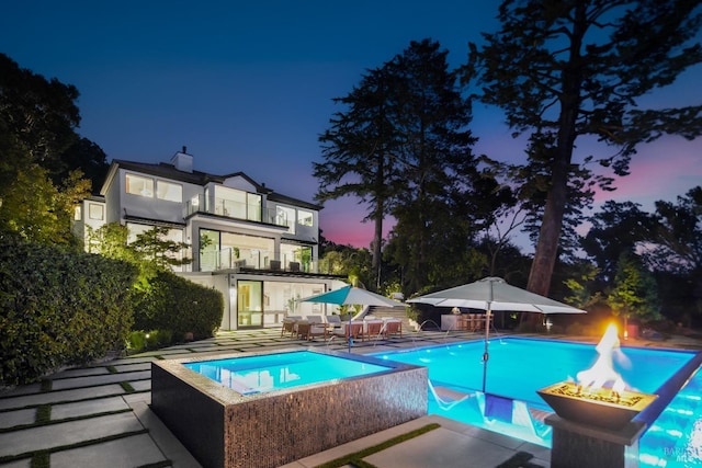 pool at dusk with an outdoor fire pit and a patio