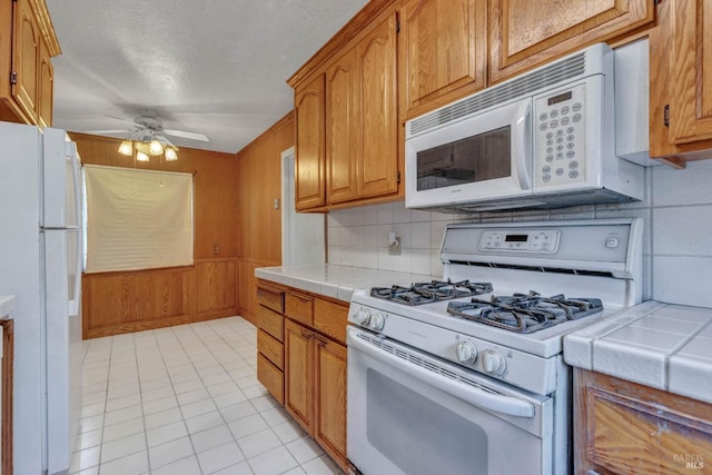 kitchen with backsplash, white appliances, light tile patterned floors, and tile counters