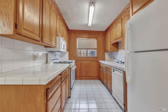 kitchen with light tile patterned floors, tile counters, decorative backsplash, white appliances, and a textured ceiling