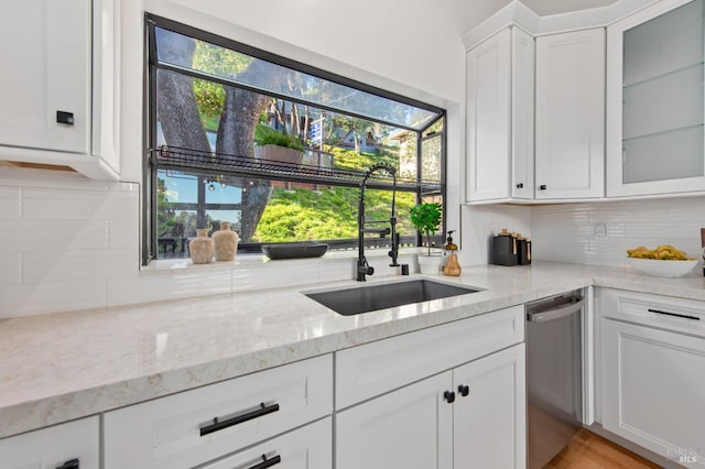 kitchen with sink, light stone counters, dishwasher, white cabinets, and backsplash