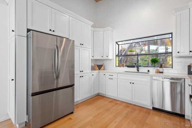 kitchen with sink, white cabinets, decorative backsplash, stainless steel appliances, and light wood-type flooring